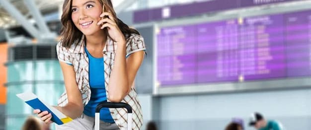 A female student posing with a passport tucked with a flight ticket talking to someone on the phone at the airport