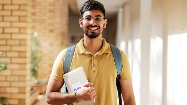 An excited male student holding books in his right hand standing in the corridor of the college.