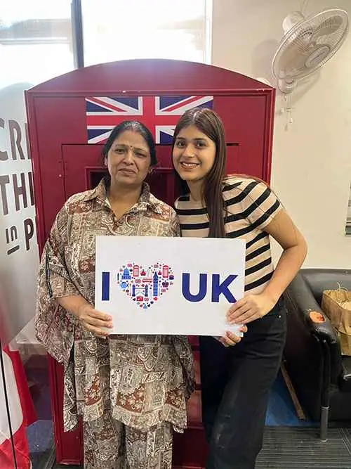 Mother-daughter duo holding I love the UK placard card in front of the Union Jack.